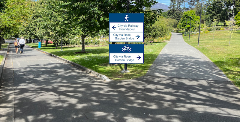A photo taken on entering the Rose Garden from the western end of the Bridge of Remembrance. A pedestrian wayfinding sign has been added which shows City via Railway Roundabout to the left and City via Rose Garden Bridge to the right. A cyclist wayfinding sign has been added which shows City via Rose Garden Bridge to the right.