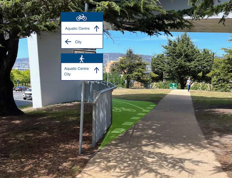 A photo of the shared path passing under the eastern end of the Bridge of Remembrance. A cyclist wayfinding sign has been added which shows Aquatic Centre straight ahead and City to the left. A pedestrian wayfinding sign has been added which shows Aquatic Centre and City straight ahead. The existing signs have been removed. Some green paint has been applied to the bike path.