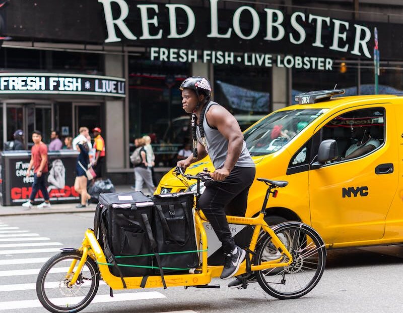 A man rides a loaded yellow cargo bike down a New York street past a yellow taxi