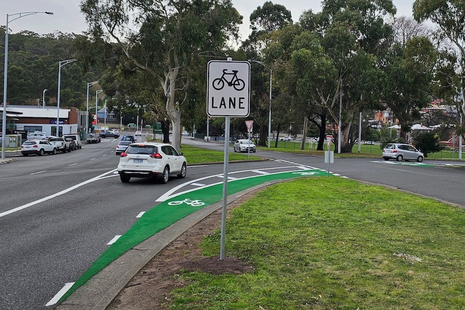 A green painted bike lane on the inside of a corner leading into an intersection. There is separation between the car lane and the bike lane but no physical barrier.
