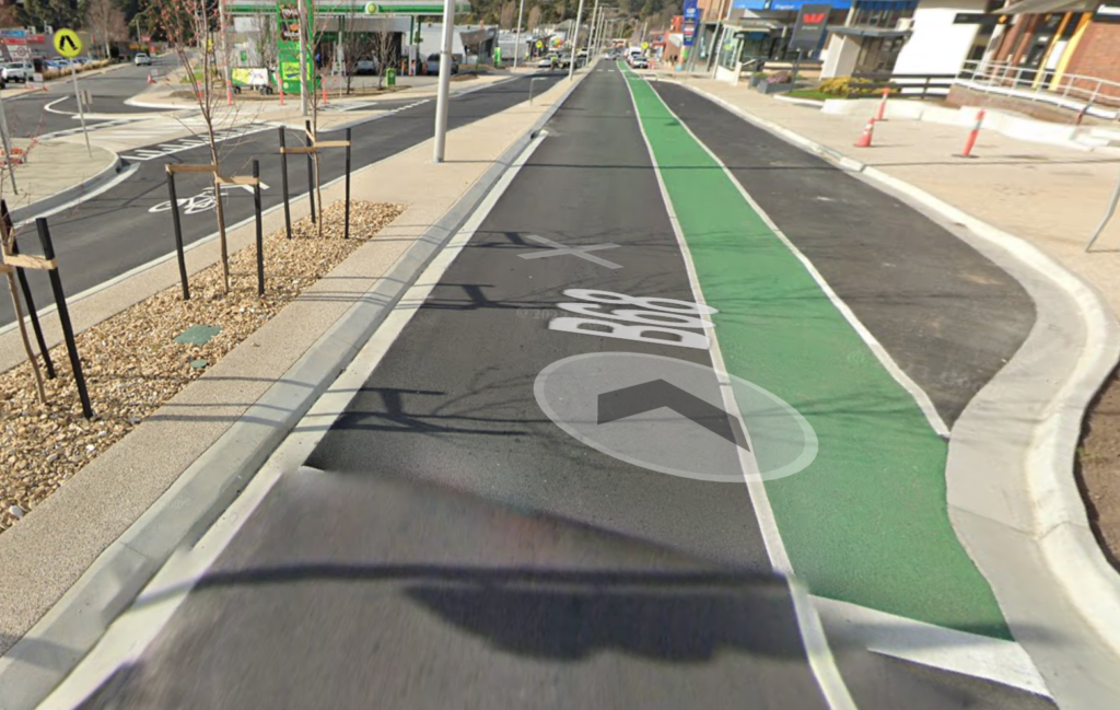 A green painted bike lane between a traffic lane and a parking bay in the Kingston CBD. The other side of the road doesn't have a bike lane. Instead there is a bike symbol painted in the middle of the traffic lane.