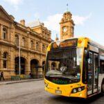 A Metro Tasmania bus leaving a bus stop in the Hobart Bus mall. The Hobart General Post Office is in the background.