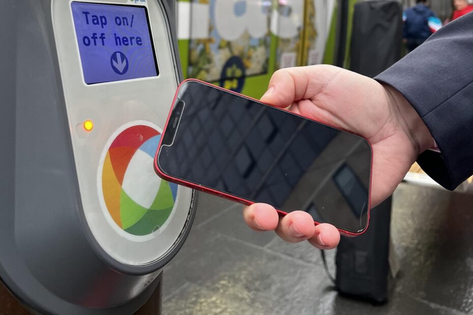 A hand holds a mobile phone towards a contactless payment reader which displays "Tap on/off here".