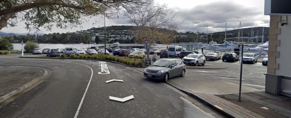 A photo showing the view approaching the Bellerive Pier from Cambridge Road. There's lots of parked cars and no pedestrian crossings.