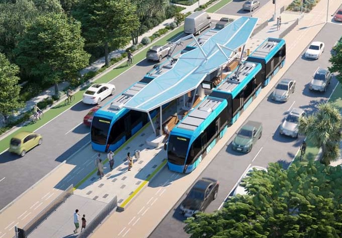 An artists impression showing two trackless trams stopped at a station. Each tram has a dedicated lane with painted lines down the middle. There are two lanes of traffic in each direction on either side of the trackless trams.