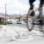 A photo showing a bike lane on Augusta Road Lenah Valley with a motion blurred person riding a bike passing in the foreground. There's moving and parked cars in the background.