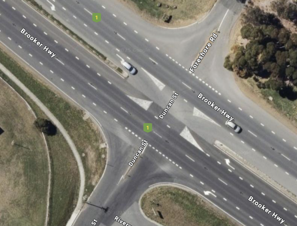 A satellite image showing the divided Brooker Highway with two lanes in each direction. Foreshore Road and Duncan Street meet the Brooker at give ways. There's various additional lanes to help with turning. There's footpath avoiding the intersection. There's no other visible infrastructure for walking or riding.